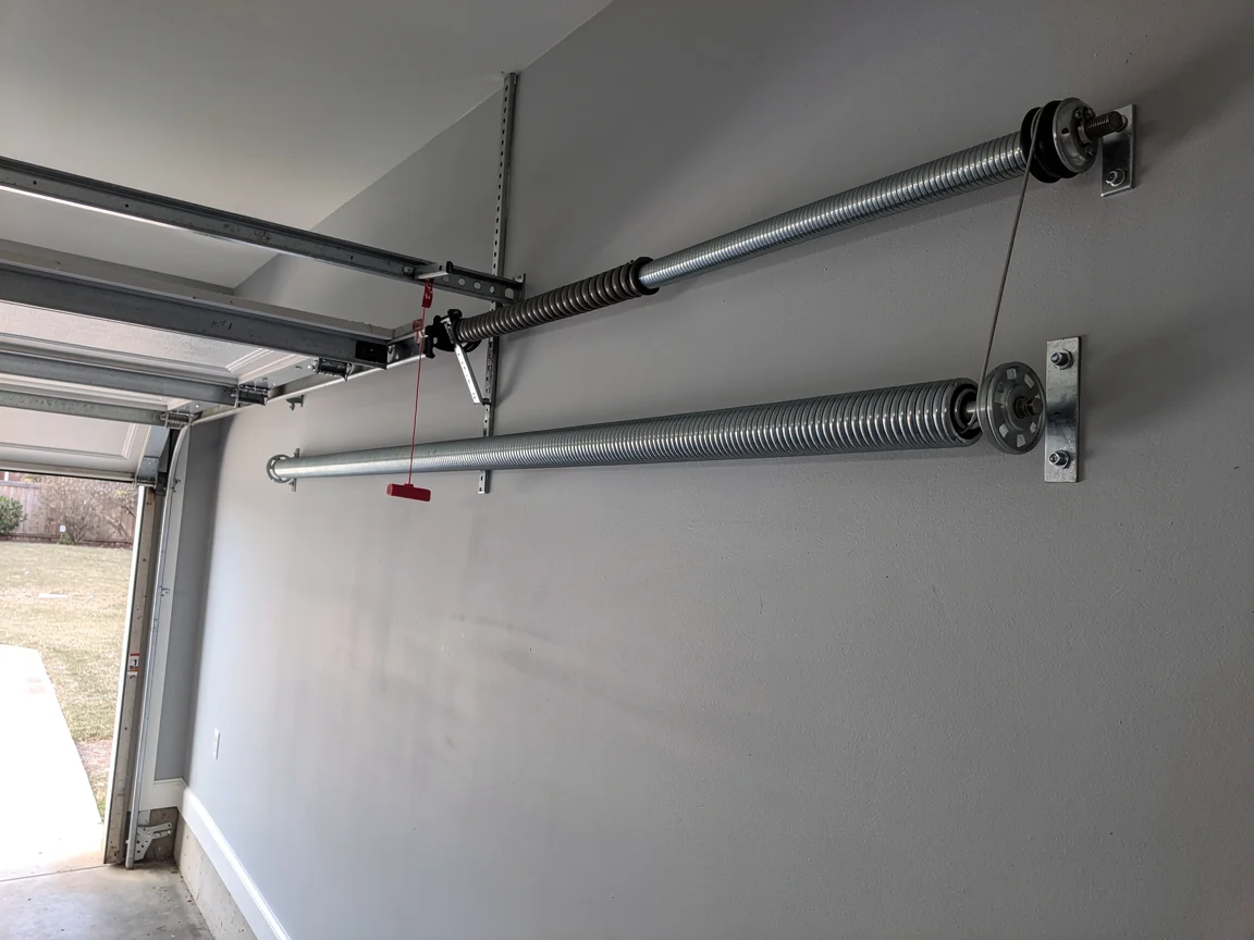 Two garage door torsion springs are mounted on a light gray wall.